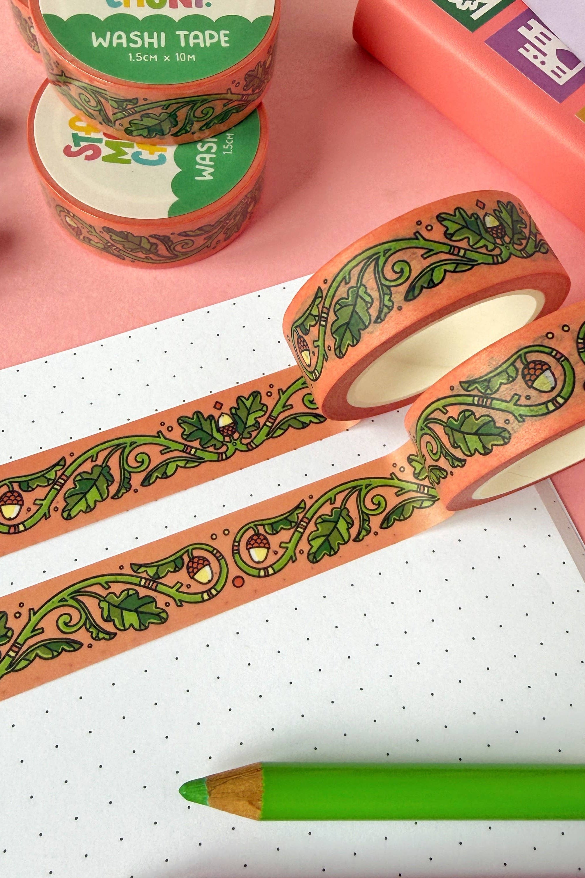 Decorative washi tape with green oak leaf patterns on a pink surface with stationery items.